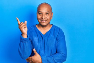 Orta yaşlı, gündelik giysiler giyen, gülümseyen, mutlu, eli ve parmağı kenarda bir orta yaşlı adam. 