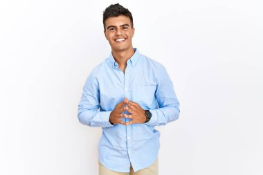 İzole edilmiş arka planda duran iş gömleği giyen genç İspanyol adam ellerini birleştirip gülümseyerek gevşemiş ve neşeli olmasını diliyordu. Başarı ve iyimserlik 