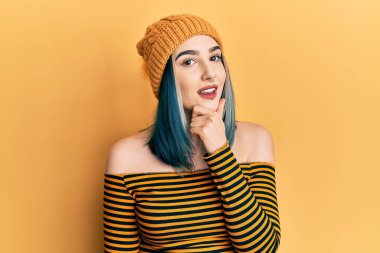 Genç modern kız yün şapka takıyor kameraya kendinden emin bakıyor kollarını kavuşturup gülümsüyor ve çenesini kaldırıyor. Olumlu düşünmek. 