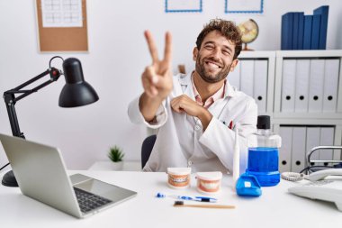 Klinikte çalışan genç İspanyol dişçi kameraya bakıp zafer işareti yaparken gülümsüyor. İki numara.. 