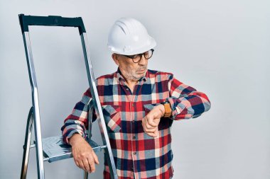 İnşaat merdivenlerine yakın, kasklı yakışıklı, kol saatini kontrol eden, rahat ve kendinden emin. 