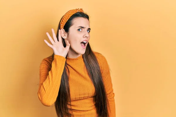 若いブルネットのティーンエイジャーは噂やゴシップへの聴聞会を聞いて耳の上に手で笑みを浮かべてカジュアルな黄色のセーターを着て 聴覚障害の概念 — ストック写真
