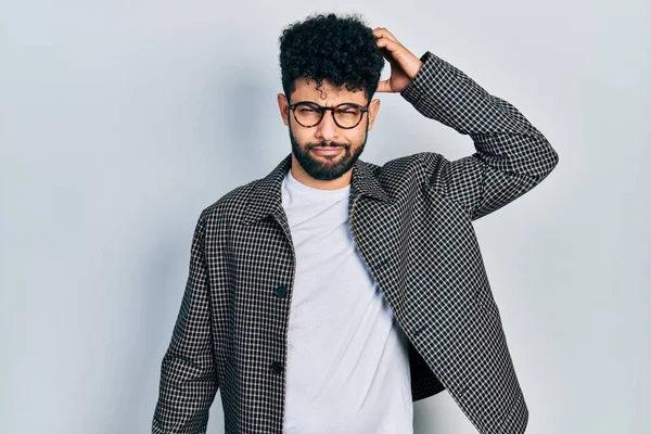 Young arab man with beard wearing glasses confuse and wonder about question. uncertain with doubt, thinking with hand on head. pensive concept.
