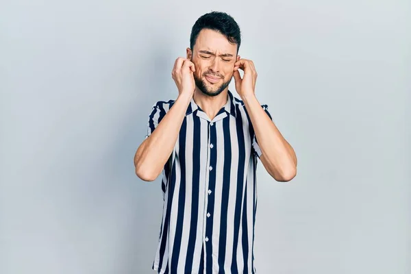 大音量の音楽のノイズのためにいらいらする表情で指で耳を覆うカジュアルな服を着た若いヒスパニック系の男 聴覚障害の概念 — ストック写真