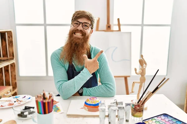 红头发的男人 留着长胡子 在艺术工作室里画着黏土碗 面带微笑 手指手画脚地朝旁边 脸上洋溢着愉快而自然的表情 — 图库照片