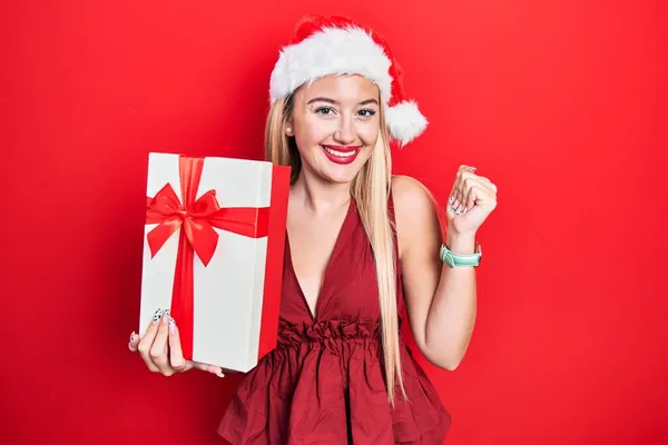 Jovem Loira Vestindo Chapéu Natal Segurando Presentes Gritando Orgulhoso Celebrando — Fotografia de Stock