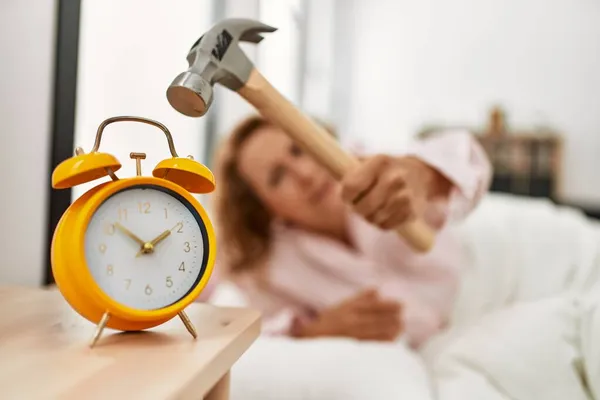 中年妇女躺在卧室床上用锤子关掉闹钟 — 图库照片