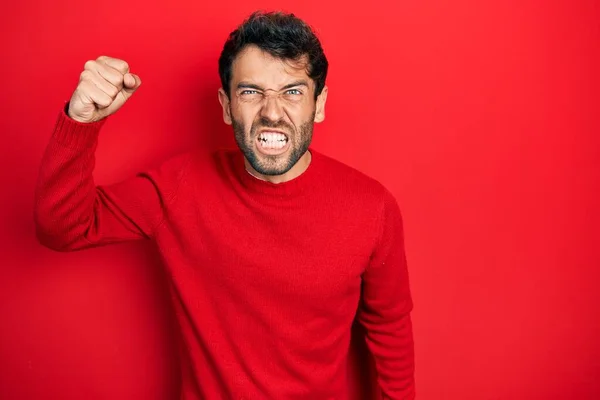 怒って怒って怒って怒って怒って怒って叫びながら拳を上げるカジュアルな赤いセーターを着て髭を生やしたハンサムな男 怒りと攻撃的な考え方 — ストック写真