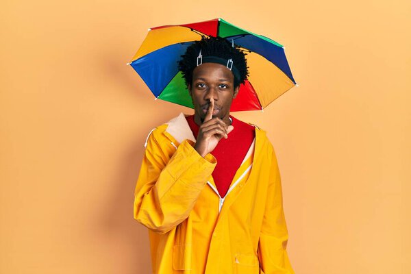 Young african american man wearing yellow raincoat asking to be quiet with finger on lips. silence and secret concept.