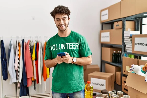 Jonge Spaanse Man Vrijwilligersuniform Gesprek Smartphone Het Liefdadigheidscentrum — Stockfoto