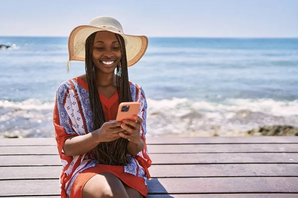 Genç Afrikalı Amerikalı turist kumsalda bankta akıllı telefon kullanıyor..