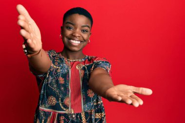 Afrikalı Amerikalı genç bir kadın kameraya sarılıp gülümseyerek gülümsüyor. Mutluluğu kucaklayan neşeli bir ifade.. 