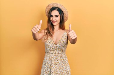 Yaz şapkası takan genç İspanyol kız elinle olumlu jest yapmayı onaylıyor, gülümsüyor ve başarı için seviniyor. kazanan jest. 