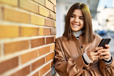 Genç, güzel esmer kadın dışarıda mutlu bir şekilde gülümsüyor akıllı telefon kullanıyor.