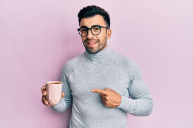 Genç İspanyol adam gözlük takıyor ve bir fincan kahve içiyor. Gülümsüyor. 