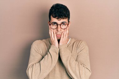 Gündelik kıyafetler ve gözlük takan genç İspanyol adam. Yüzü, depresyonu ve üzüntüyü örten yorgun eller. 
