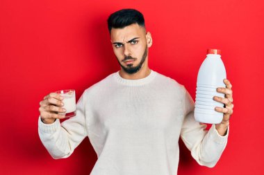 Sakallı, elinde bir bardak süt ve plastik şişe tutan, kafası karışık bir İspanyol. şüphe kavramı. 