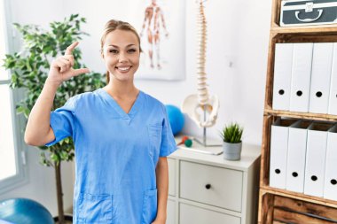 Ağrı giderme kliniğinde çalışan beyaz bir kadın gülümsüyor ve el hareketleriyle el hareketleriyle küçük boy işareti yapıyor, parmaklarına bakıyor ve kameraya bakıyor. ölçüm kavramı. 