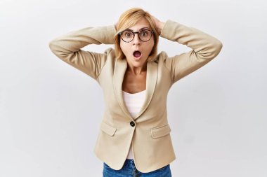 Orta yaşlı sarışın iş kadını, izole edilmiş arka planda duruyor. Deli ve korkmuş, elleri başının üstünde, korkmuş ve ağzı açık bir şekilde şok geçirmekten korkan. 