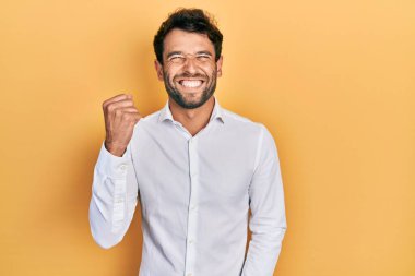 Sakallı, sıradan beyaz tişörtlü yakışıklı adam kolları havada ve gözleri kapalı bir şekilde başarıyı kutluyor. 