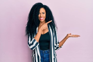 Orta yaşlı Afro-Amerikalı kadın gündelik giysiler giyip kameraya hayret ediyor ve gülümsüyor.. 