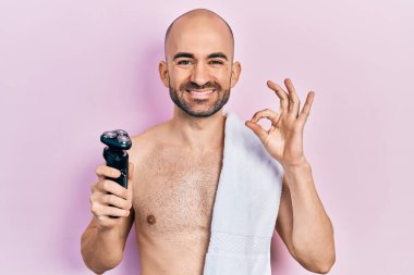 Tıraş bıçağı tutan kel genç adam parmaklarıyla imza atıyor, gülümsüyor ve mükemmel bir sembol oluşturuyor. 