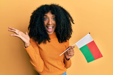 Afro saçlı Afro-Amerikalı kadın elinde madagaskar bayrağı ile başarıyı mutlu bir gülümsemeyle ve kazanan ifadeyle kutluyor. 