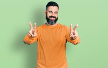 Sakallı, sıradan bir kazak giyen, ağzı açık gülümseyen, iki elini de zafer işareti yapan İspanyol bir adam. İki numara.. 