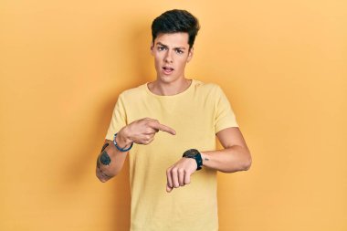 Gündelik sarı tişört giyen genç İspanyol adam acele edip saati, sabırsızlığı ve gecikmeye kızmayı işaret ediyor. 