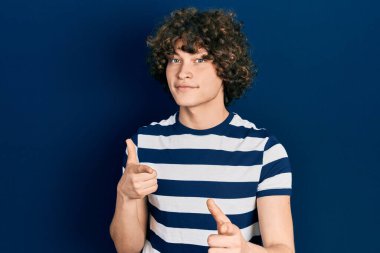 Sıradan çizgili tişört giyen yakışıklı genç adam mutlu ve komik yüzüyle kamerayı işaret ediyor. iyi enerji ve titreşimler. 