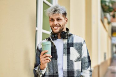 Genç İspanyol adam şehirde kahve içerken kulaklık takıyor..