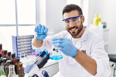 Genç İspanyol adam bilim adamı üniforması giyiyor. Laboratuvarda sıvı karıştırıyor.