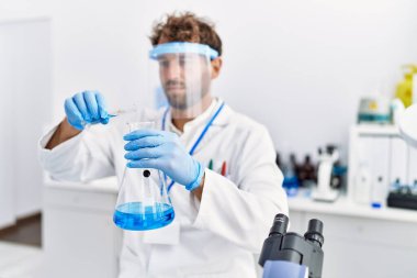 Laboratuvarda deney tüpü tutan bilim adamı üniforması giyen İspanyol genç adam.