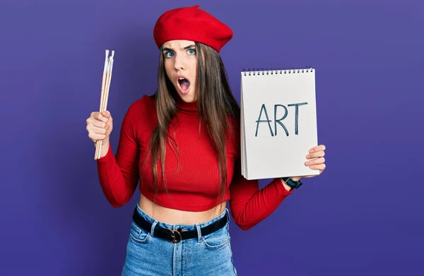 Young Brunette Teenager Holding Art Notebook Paintbrushes Afraid Shocked Surprise — Stock Photo, Image