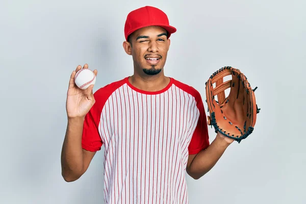 Joven Hombre Afroamericano Con Uniforme Béisbol Sosteniendo Guante Bola Guiñando —  Fotos de Stock