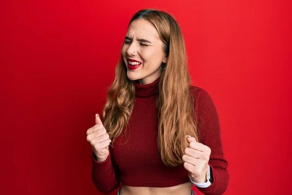 腕を上げて成功のために興奮したタートルネックセーターを身に着けている若いブロンドの女性が育ち 目は勝利笑顔を祝う閉じました 勝者のコンセプト — ストック写真