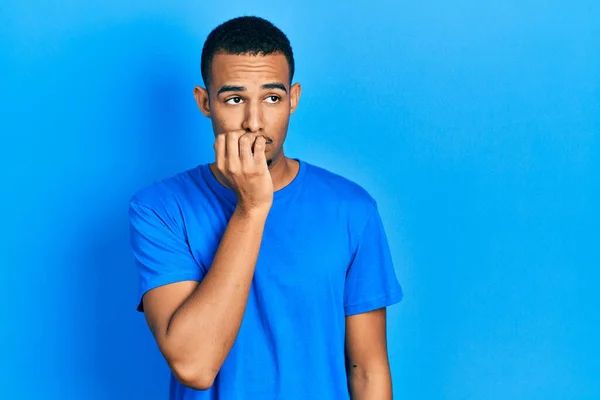 若いアフリカ系アメリカ人の男性が口の爪をかむ上で手でストレスと神経を見てカジュアルな青のTシャツを着ている 不安の問題 — ストック写真