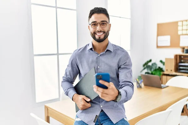 Young arab man smiling confident using smartphone at office