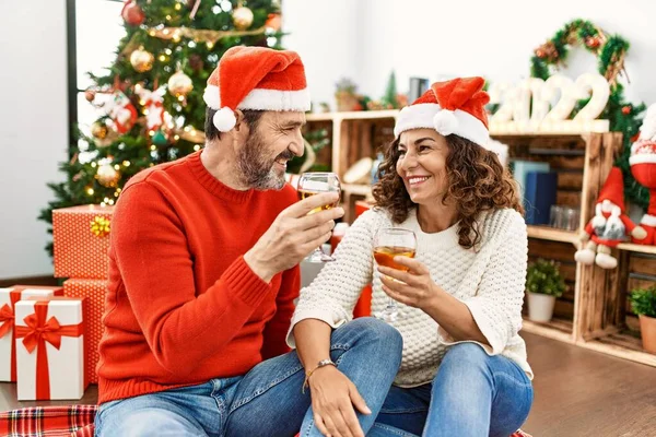中世のヒスパニック夫婦はクリスマスの帽子をかぶっている 床に座り 自宅でシャンパンで乾杯 — ストック写真