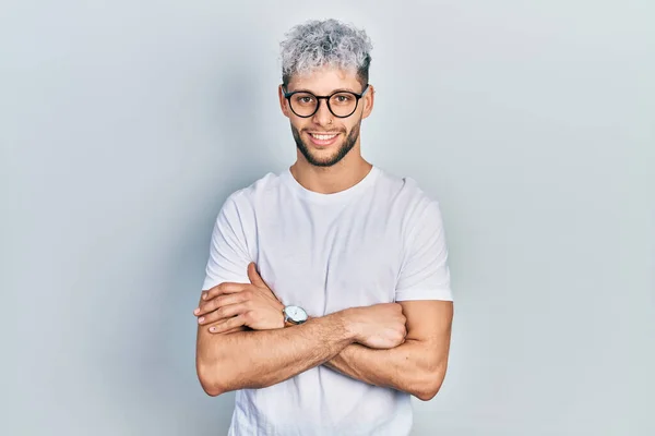 Young hispanic man with modern dyed hair wearing white t shirt and glasses happy face smiling with crossed arms looking at the camera. positive person.