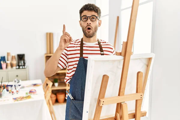 在艺术工作室里的阿拉伯年轻人惊奇而惊奇地抬起头 用手指和胳膊指指着 — 图库照片