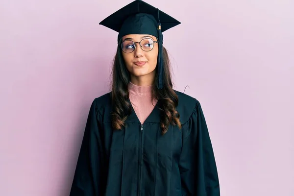 卒業キャップと式のローブを着た若いヒスパニック系の女性が笑顔で横を見て 離れて考えて見つめて — ストック写真