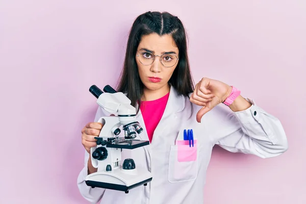 Jovem Hispânica Vestindo Uniforme Cientista Segurando Microscópio Com Rosto Irritado — Fotografia de Stock