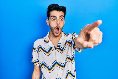 Gündelik giysiler giymiş genç İspanyol bir adam parmağıyla işaret ederek şaşırmış, ağzı açık, şaşırmış, ön tarafta bir şey var. 