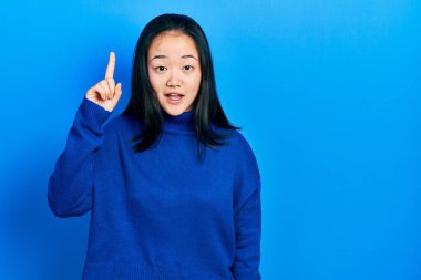 Gündelik giysiler giyen genç Çinli kız başarılı bir fikri işaret ediyor. Heyecanlı ve mutlu. Bir numara.. 