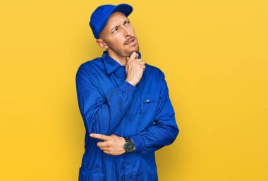 Sakallı, inşaatçı kıyafetli kel bir adam bir soru hakkında endişeli ve gergin bir şekilde düşünüyor. 