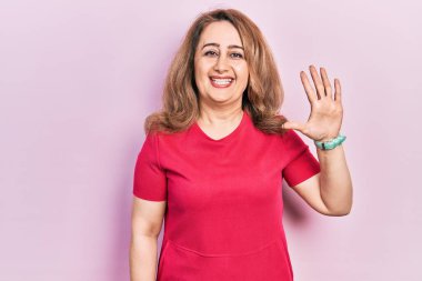 Orta yaşlı, beyaz, günlük kıyafetler giyen, beş numaralı parmaklarıyla işaret eden, kendinden emin ve mutlu bir kadın.. 