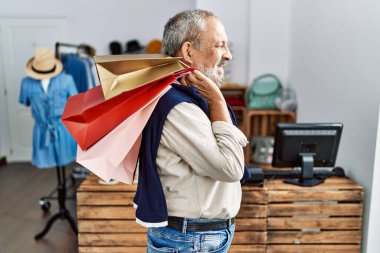 Butik dükkanında alışveriş torbaları tutan yakışıklı bir adam. Yan tarafa bakıyor, profil pozu veriyor. Doğal bir yüzü ve kendine güvenen bir gülümsemesi var.. 