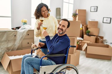 Orta yaşlı İspanyol çift şampanyayla kadeh kaldırıyor. Tekerlekli sandalyede oturan bir adam ve yeni evinde ayakları üzerinde duran bir köpek.