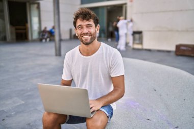 Sokakta dizüstü bilgisayar kullanarak gülümseyen İspanyol genç adam.